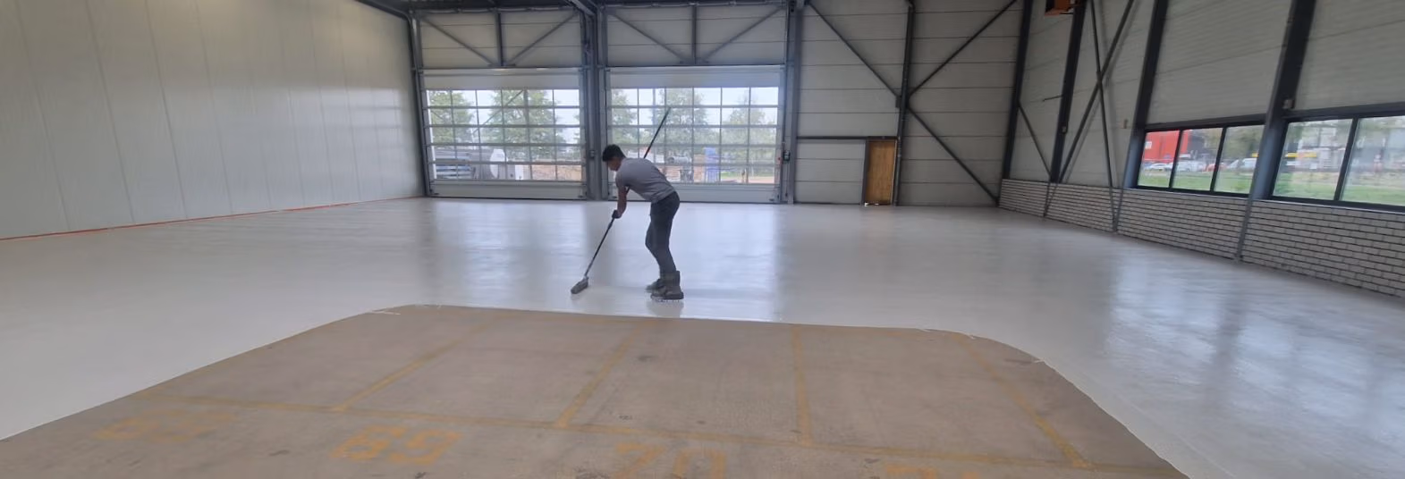 Vakman is bezig met het coaten van een betonvloer