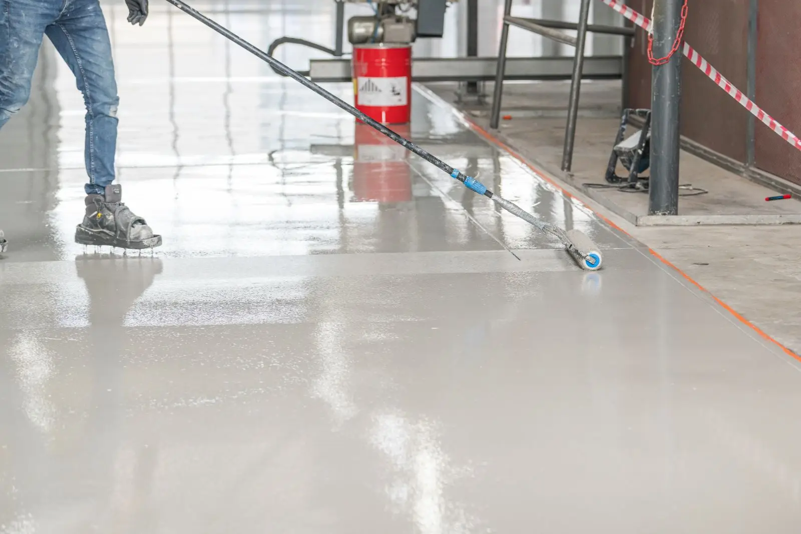 Vakman brengt egalisatielaag aan met verfroller op een geprepareerde cementdekvloer in een werkplaats.