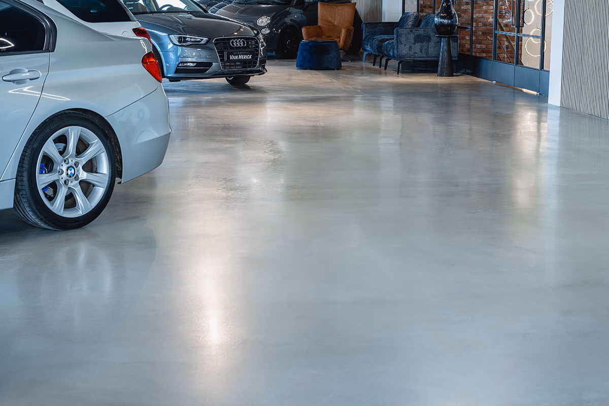 Verschillende auto's staan geparkeerd op een gepolijste betonvloer in een moderne showroom, met wat zitplaatsen en een stijlvol decor zichtbaar op de achtergrond.