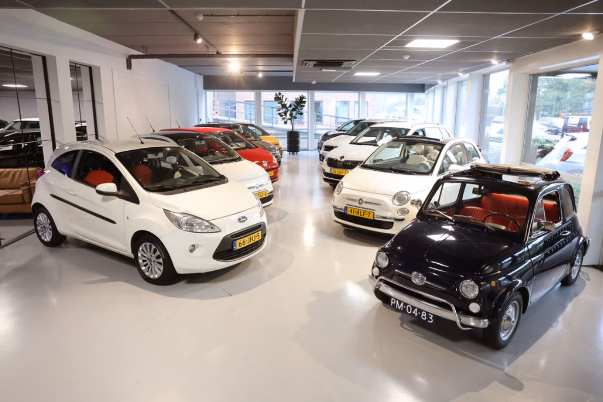 Verschillende auto's staan geparkeerd op een gepolijste betonvloer in een moderne showroom, met wat zitplaatsen en een stijlvol decor zichtbaar op de achtergrond.